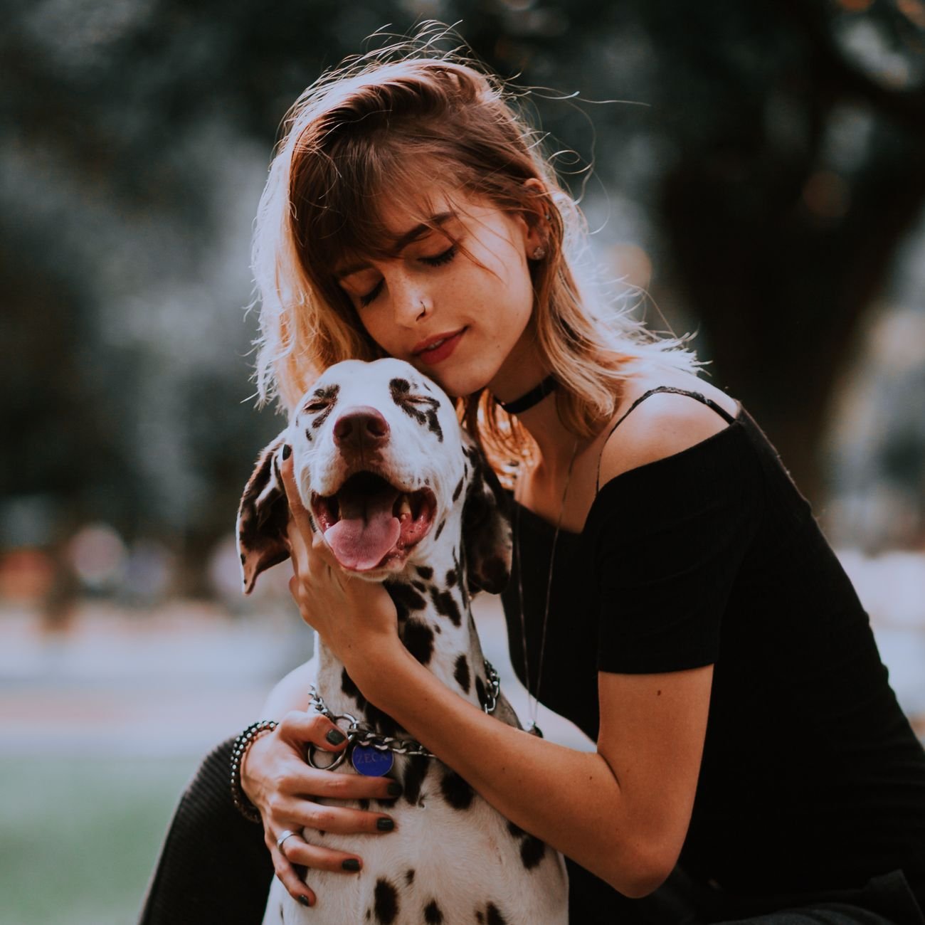 A young woman hugging her Dalmatian dog in a park.